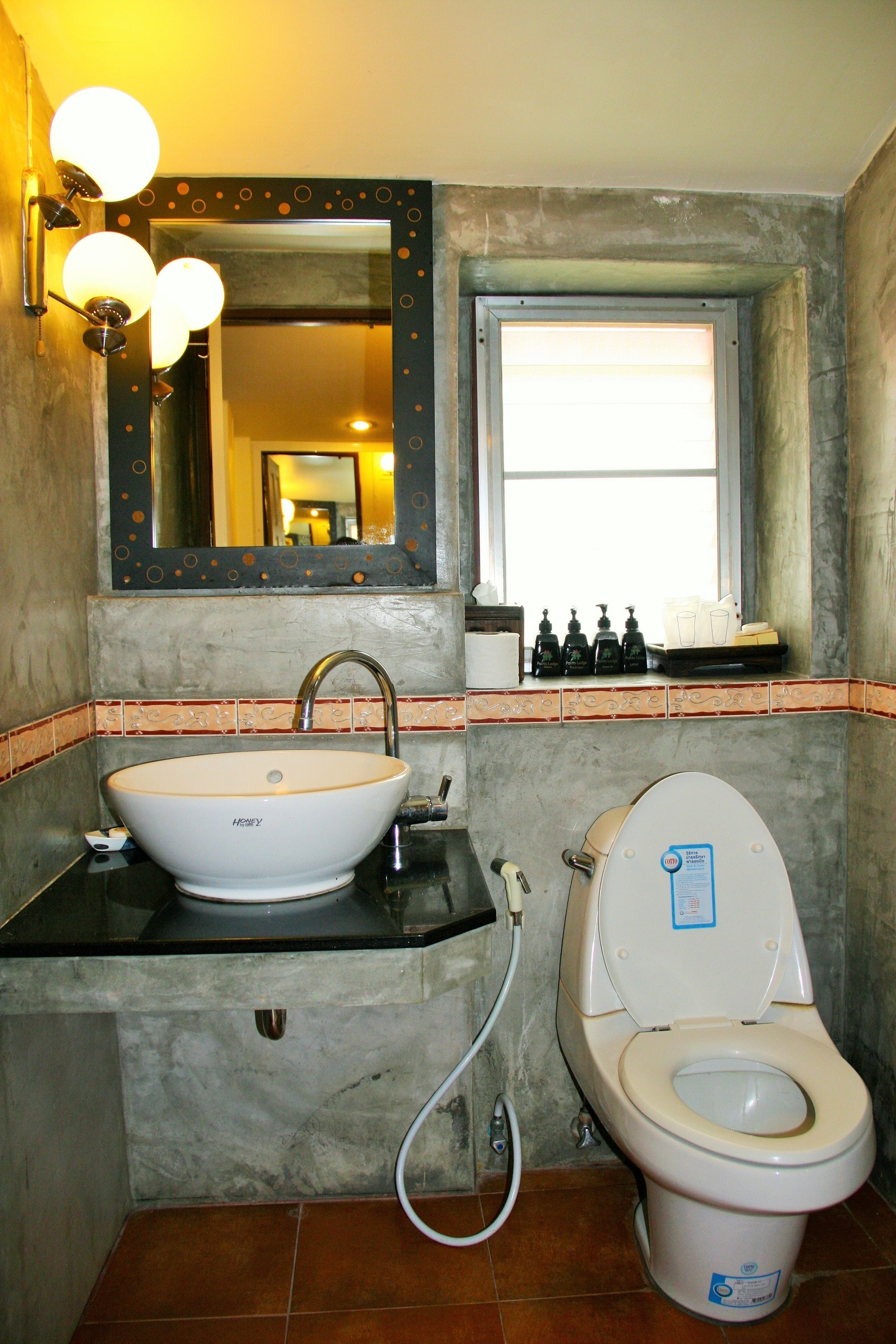 A bathroom with a white sink, a toilet, a mirror with decorative lights, and a window.