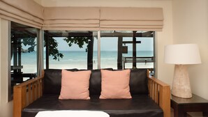 A room with a view of the beach, a sofa with cushions, and a table with a lamp.