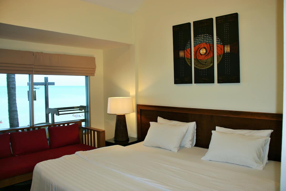 A hotel room with a large bed, a red sofa, a window with a view, and a wall with three artworks.