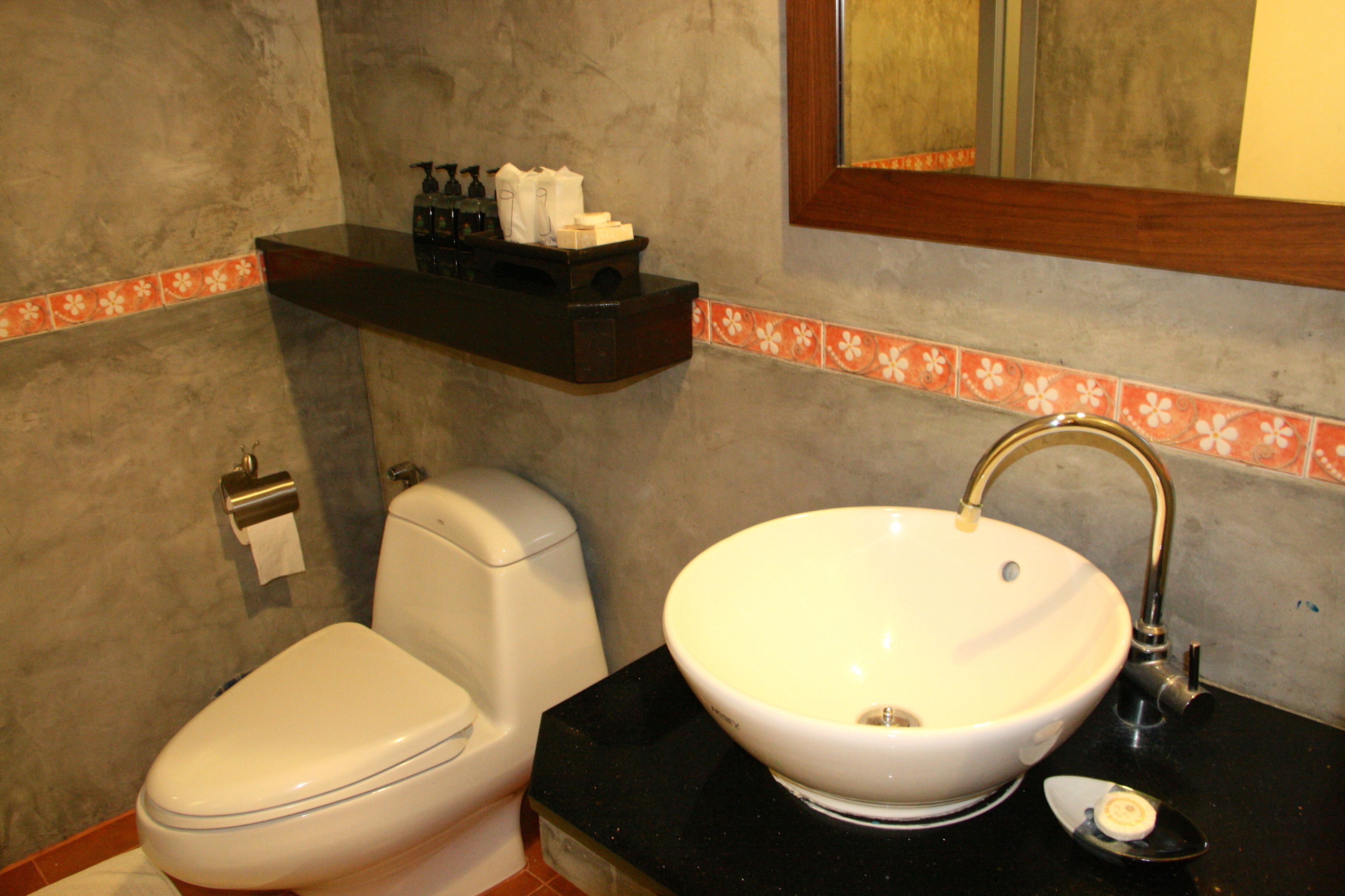 A bathroom with a white toilet, a white sink with a gold faucet, and a shelf with toiletries.
