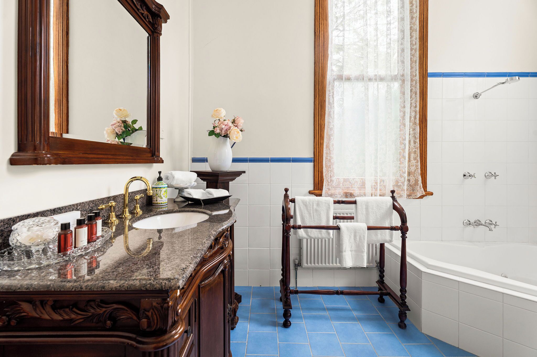 A bathroom with a wooden bathtub, a large mirror, a marble sink, and a vase with flowers.