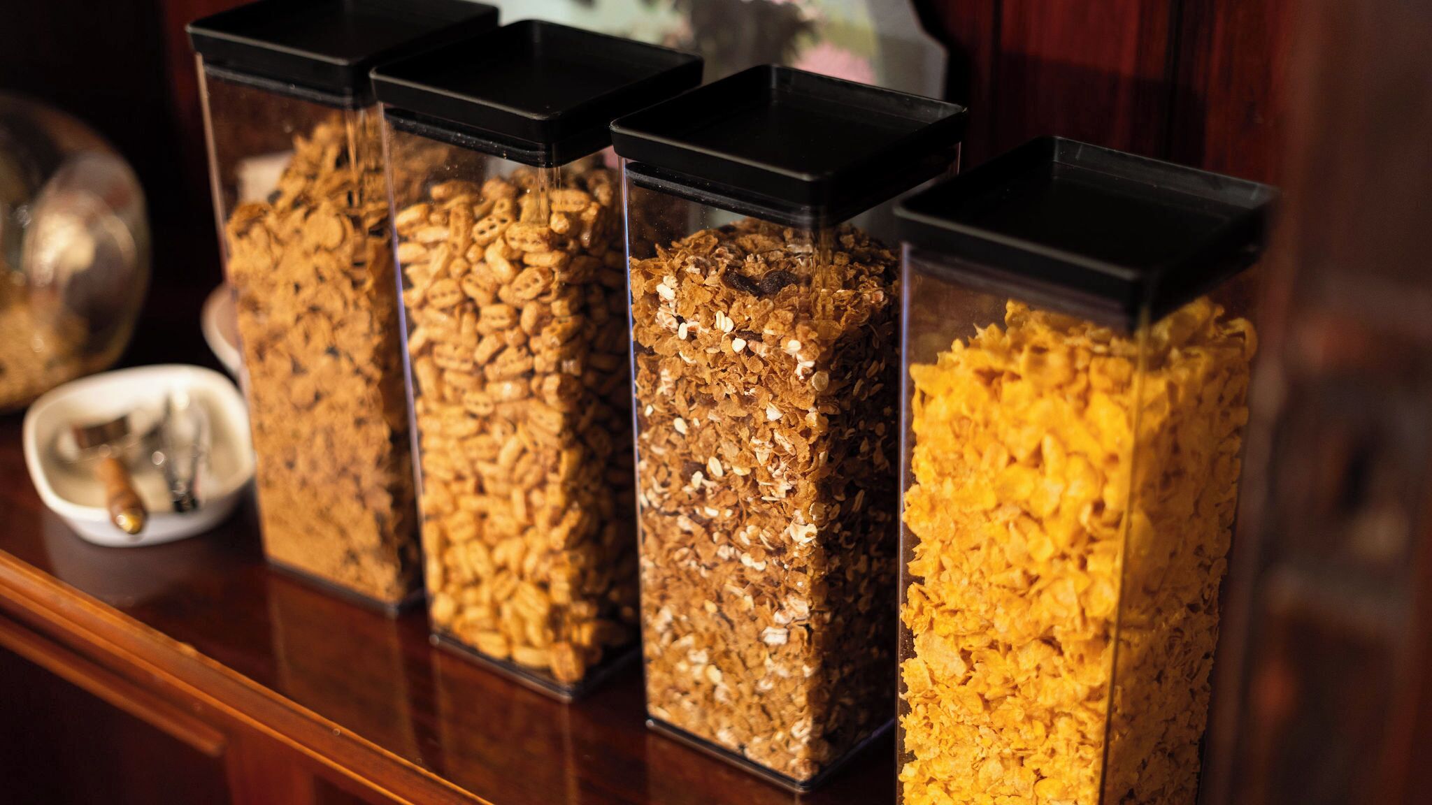 Quattro contenitori trasparenti con diversi tipi di cereali su un piano di legno.