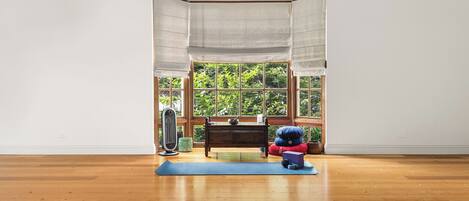 Una habitación con piso de madera, ventana con vista a follaje, un escritorio con silla y una esterilla de yoga.