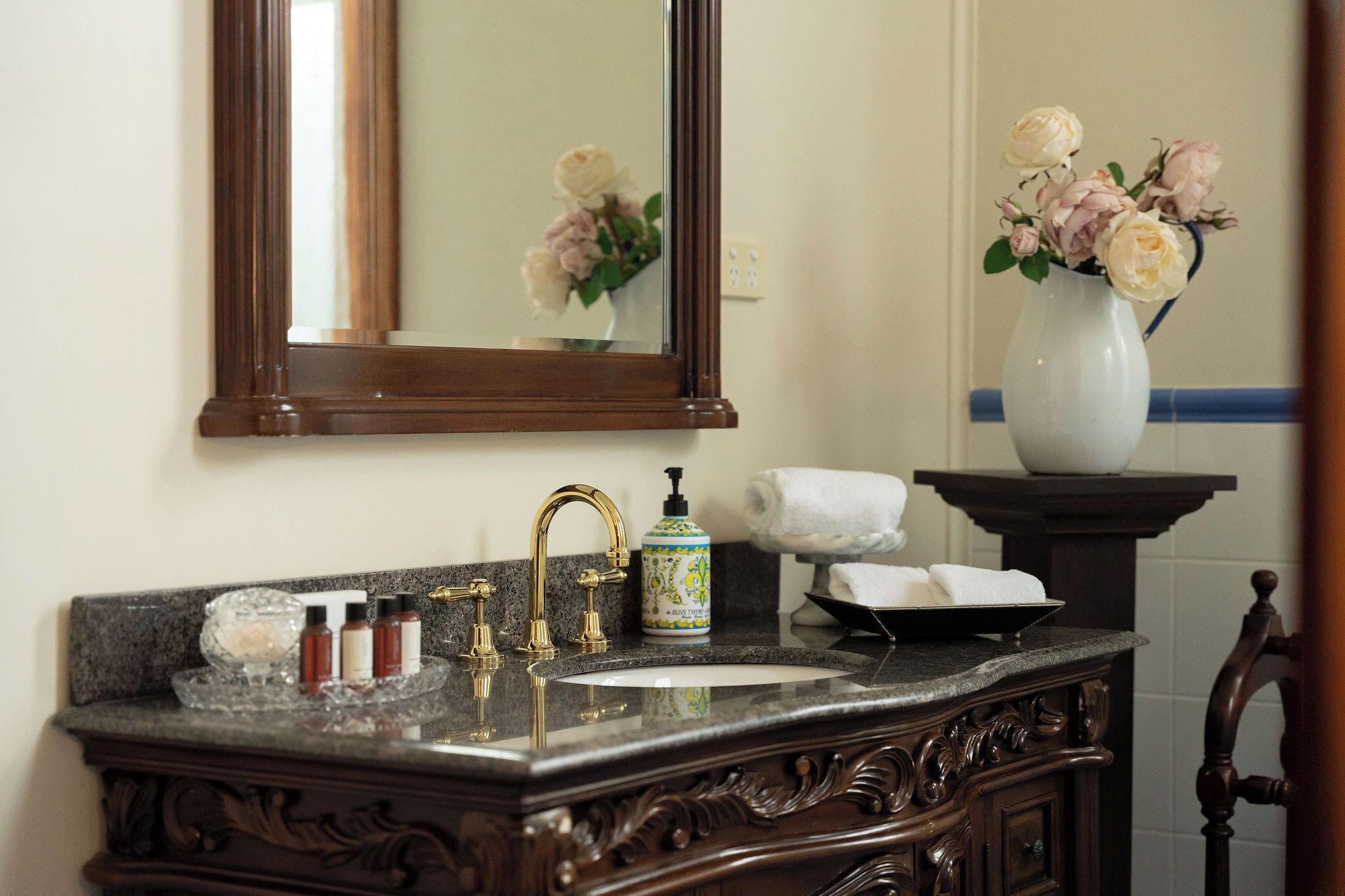 Une salle de bain avec un lavabo en marbre, des robinets dorés, un miroir, un vase avec des fleurs et un porte-serviettes.