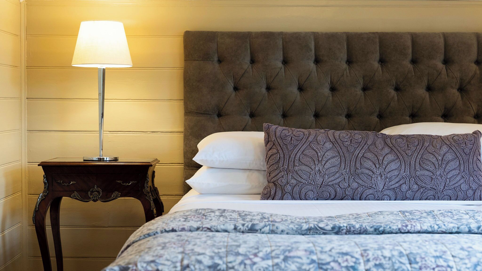 A bed with a tufted headboard, a bedside lamp, and patterned pillows.