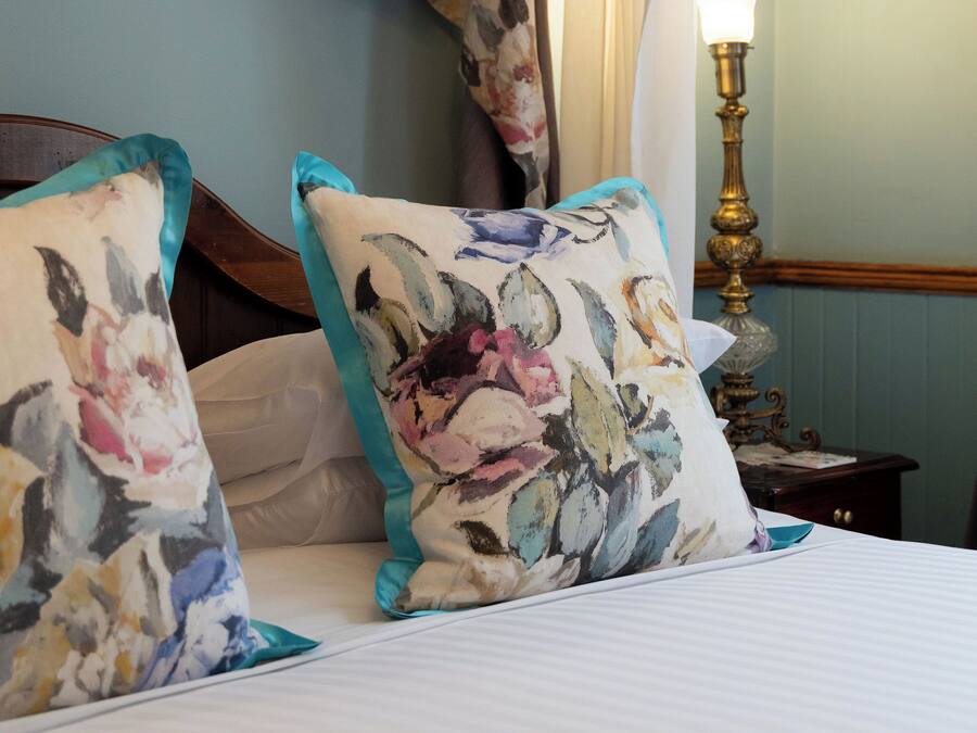 A bedroom with a canopy bed, floral-patterned pillows, a bedside table with a lamp, and a mirror.