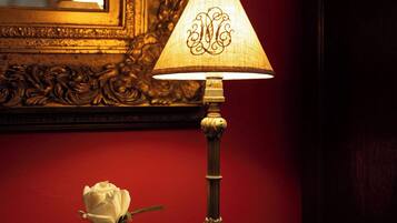 A lamp with a decorative shade, a vase with a single white rose, and a mirror with an ornate frame.