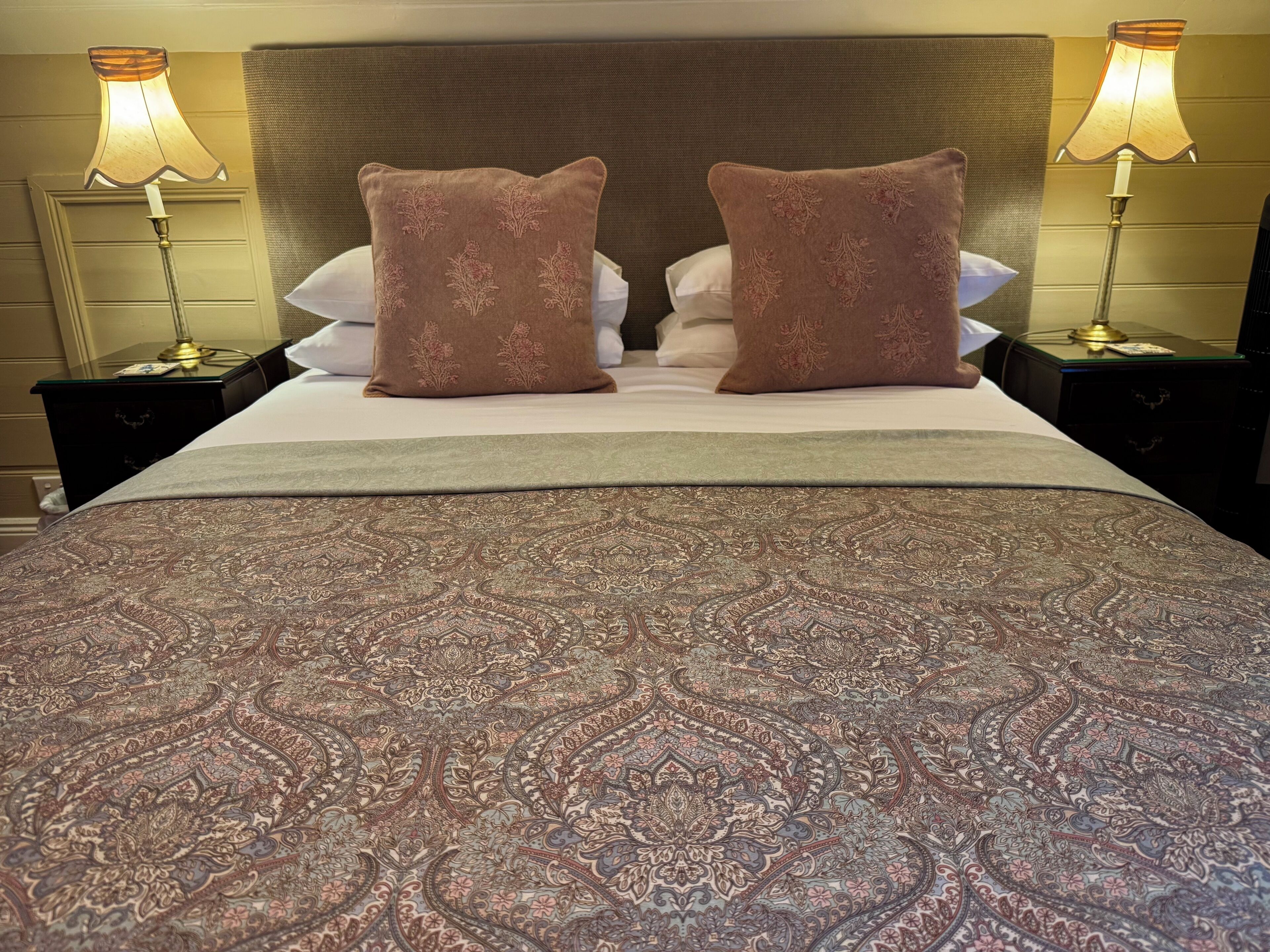 A bed with a patterned bedspread, two decorative pillows, and two bedside lamps.