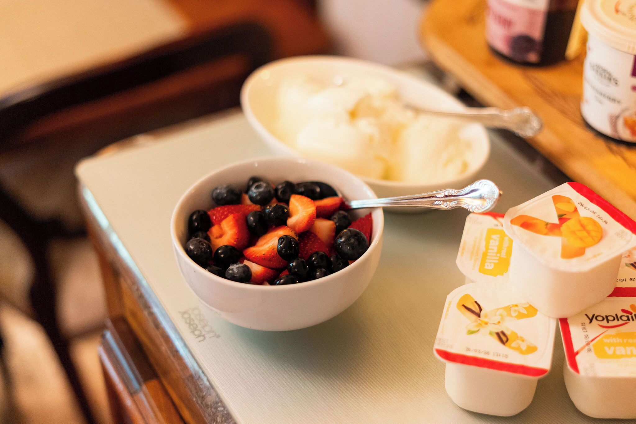 A breakfast tray with a bowl of mixed berries, a scoop of ice cream, and two containers of yogurt.