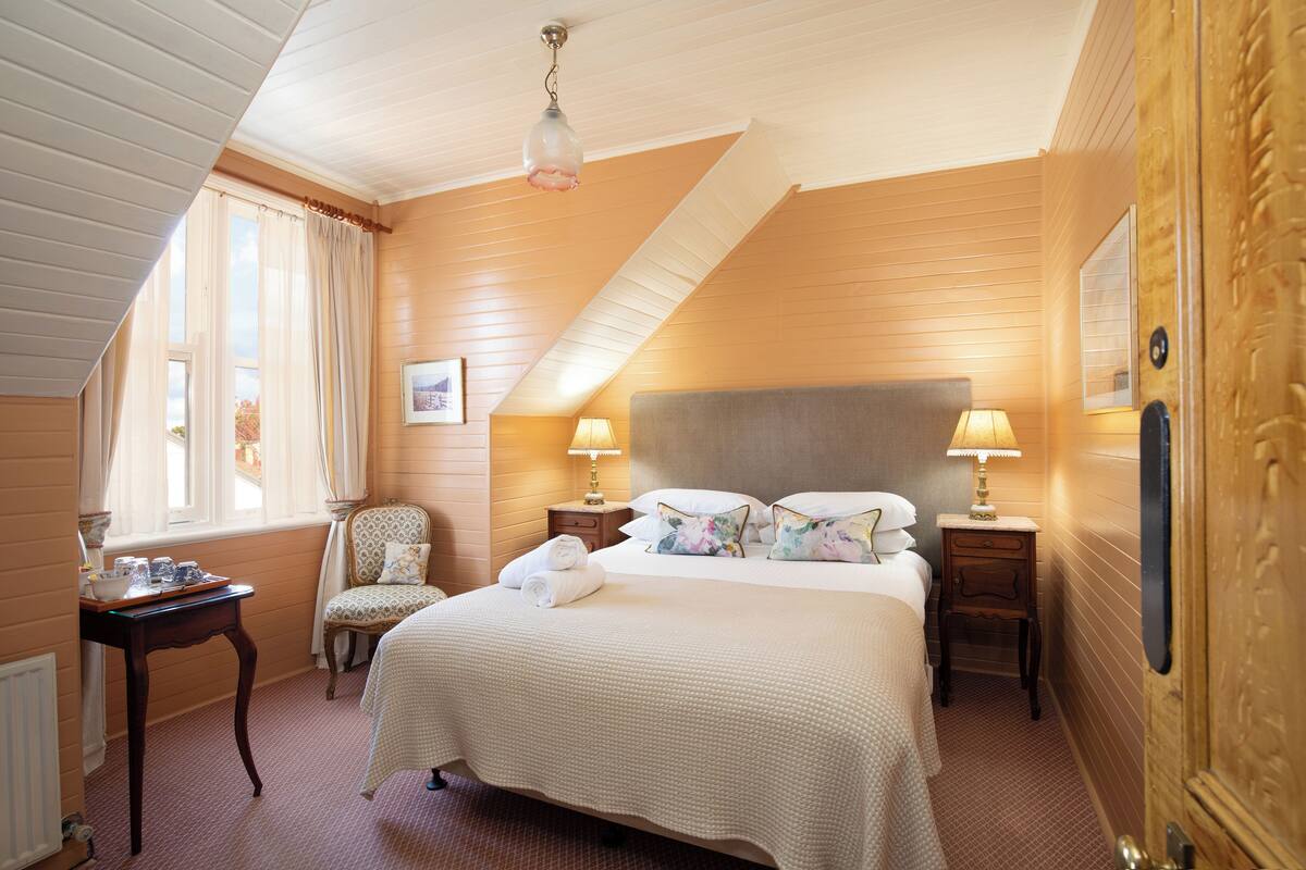 Une chambre d’hôtel avec un grand lit, deux tables de chevet avec des lampes, une chaise et une fenêtre avec des rideaux.