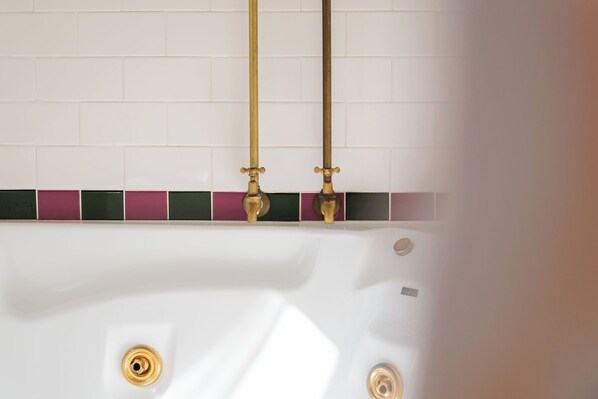 A bathtub with two gold faucets, a white tiled wall, and a green and purple tile border. - Kurrara Historic Guest House (Katoomba)