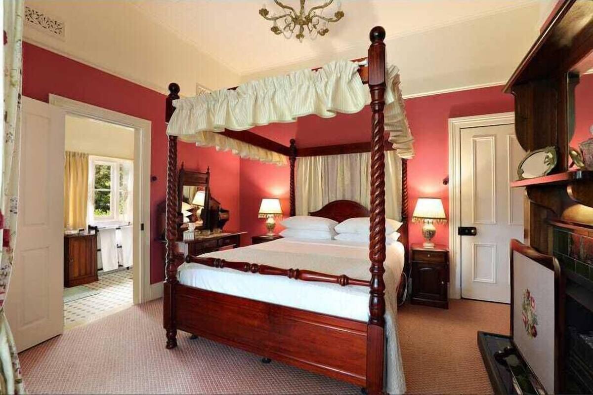 Un lit à baldaquin, une table de chevet en bois avec une lampe, une commode et un miroir.
