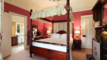 A four-poster bed with a canopy, a wooden nightstand with a lamp, a dresser, and a mirror.