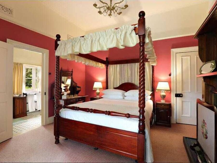 A four-poster bed with a canopy, a wooden nightstand with a lamp, a dresser, and a mirror.
