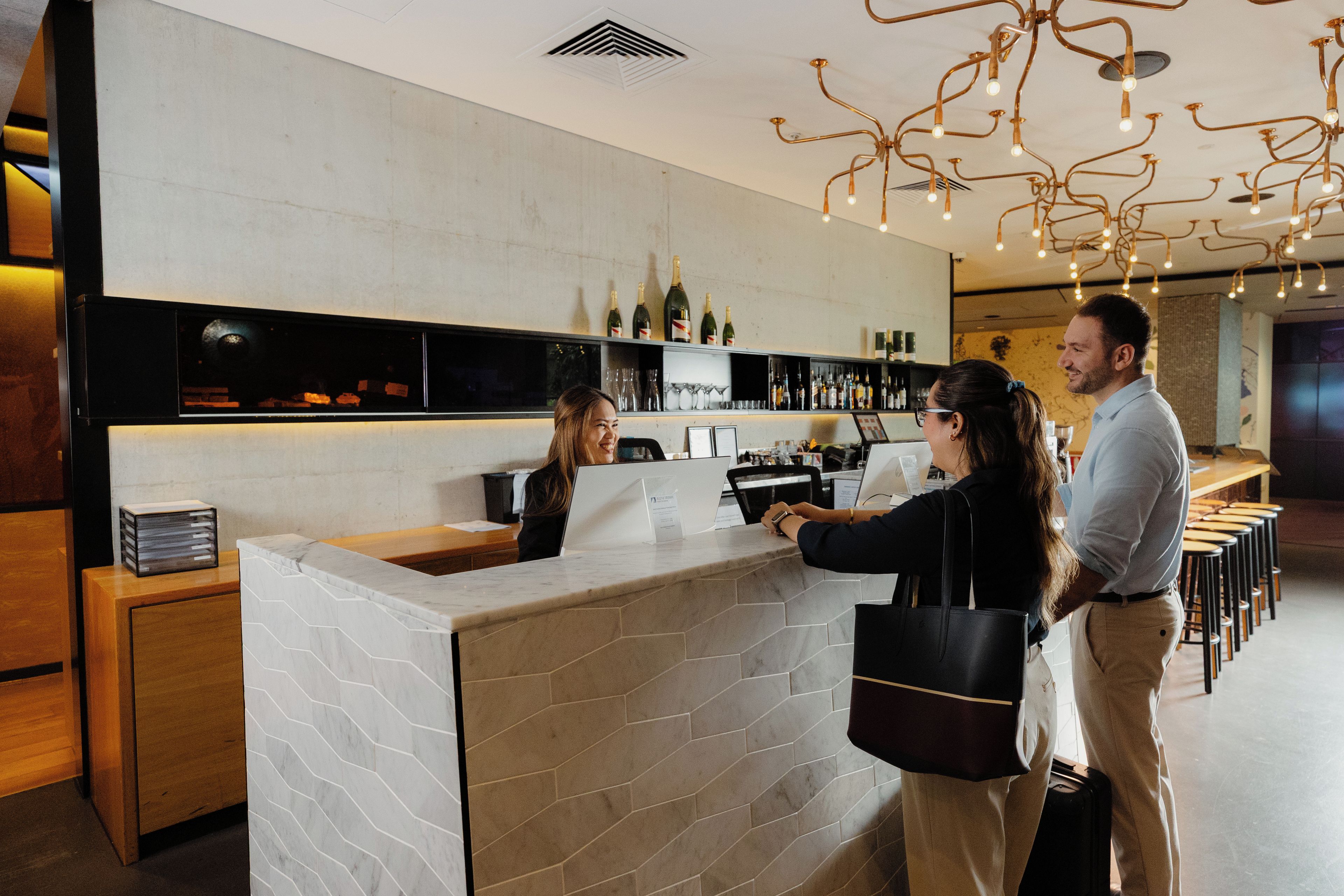 A bar area with a marble counter, shelves with bottles, and a modern light fixture.
