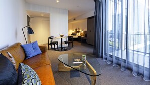 A modern living room with a leather sofa, a glass coffee table, and a dining area with chairs. - Alpha Mosaic Hotel Fortitude Valley (Fortitude Valley)