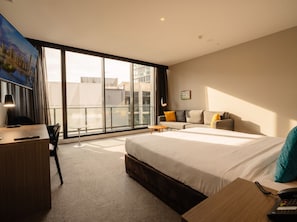A modern hotel room with a large bed, a desk, a chair, and a view of the city through floor-to-ceiling windows. - Alpha Mosaic Hotel Fortitude Valley (Fortitude Valley)