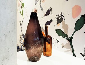A vase and a bottle on a table with a wall featuring botanical illustrations. - Alpha Mosaic Hotel Fortitude Valley (Fortitude Valley)