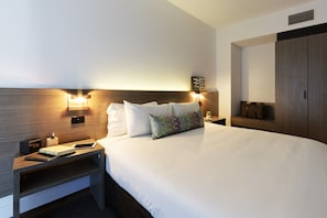 Ein Hotelzimmer mit einem großen Bett, Nachttischen, einem Kleiderschrank und Wandleuchten.