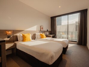 A hotel room with two beds, a desk, a chair, a nightstand, a lamp, and a large window with curtains. - Alpha Mosaic Hotel Fortitude Valley (Fortitude Valley)