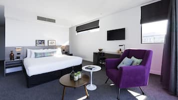 A hotel room with a bed, a desk, a purple armchair, and a small round table.
