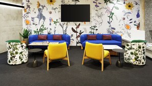 Una sala de estar moderna con dos sofás azules, sillas amarillas y un televisor de pantalla plana montado en la pared.