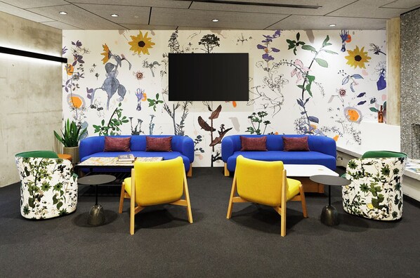 A modern living room with two blue sofas, yellow chairs, and a flat-screen TV mounted on the wall. - Alpha Mosaic Hotel Fortitude Valley (Fortitude Valley)