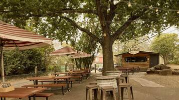 An outdoor dining area with wooden tables and benches, string lights, and a building labeled "Herbs Backyard."