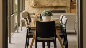 Uma área de jantar moderna com parede de pedra, televisão de tela plana e planta em vaso sobre a mesa.