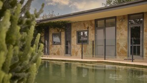 Um edifício moderno com fachada de pedra, janelas amplas e piscina em primeiro plano.