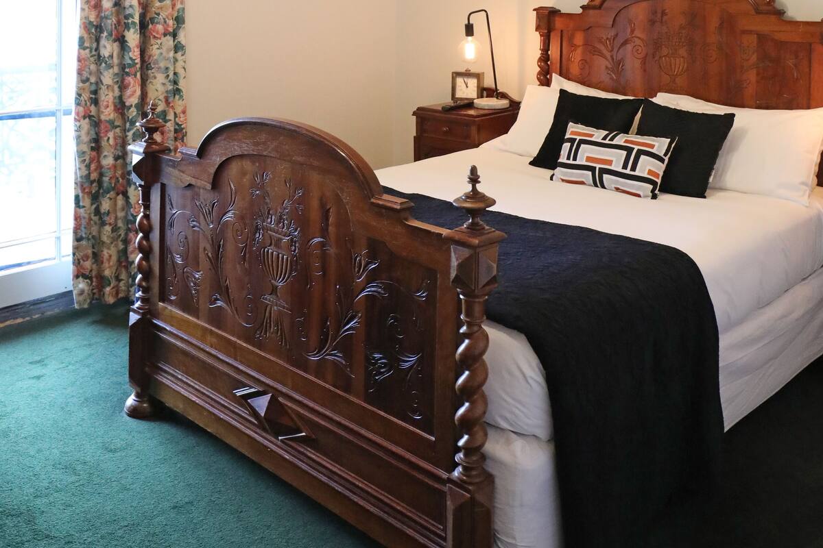 Une chambre à coucher avec un lit en bois, une table de chevet, une lampe et une fenêtre avec des rideaux.