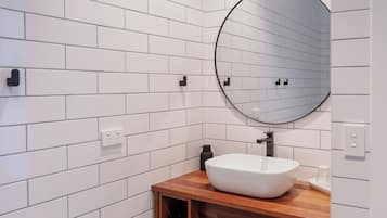 Un baño con azulejos blancos tipo metro, un espejo redondo, tocador de madera y lavabo blanco.