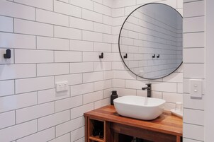 Un baño con azulejos blancos tipo metro, un espejo redondo, tocador de madera y lavabo blanco.