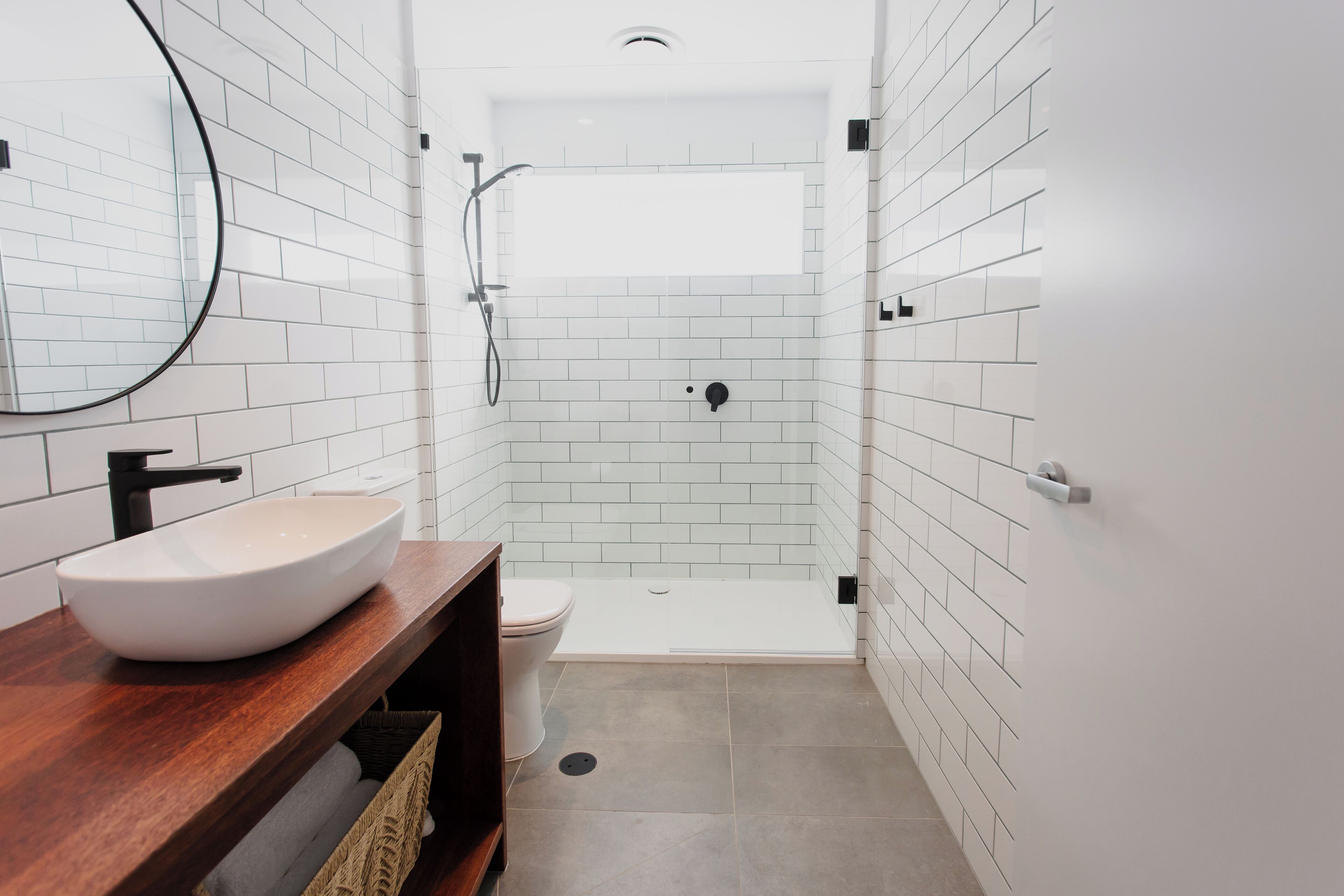 A modern bathroom with a white-tiled shower, a wooden vanity with a white sink, and a toilet.