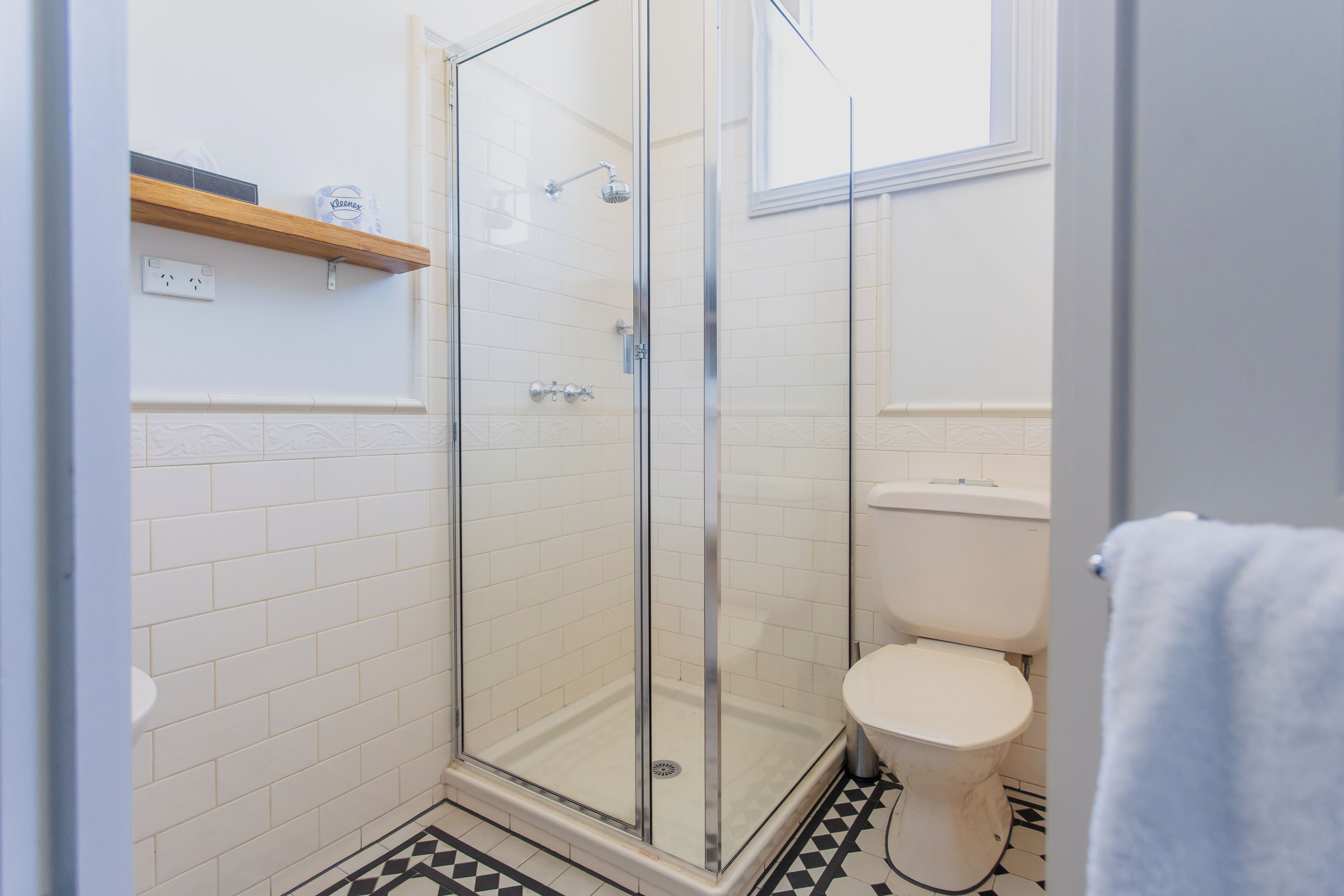 A bathroom with a glass-enclosed shower, a toilet, and a shelf with toiletries.