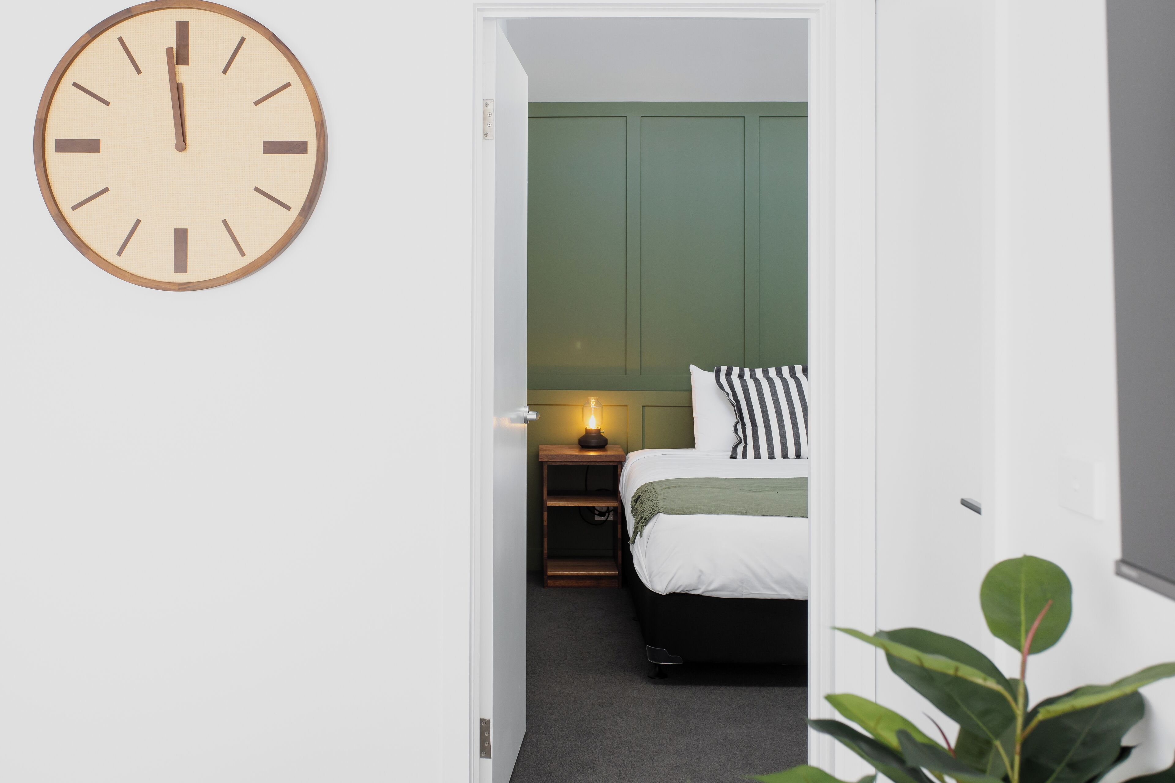 Et soveværelse med en seng, et natbord, en lampe og et vægur.