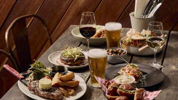 A wooden table set with various dishes, including steak, fries, and salad, along with multiple glasses of beer and wine.