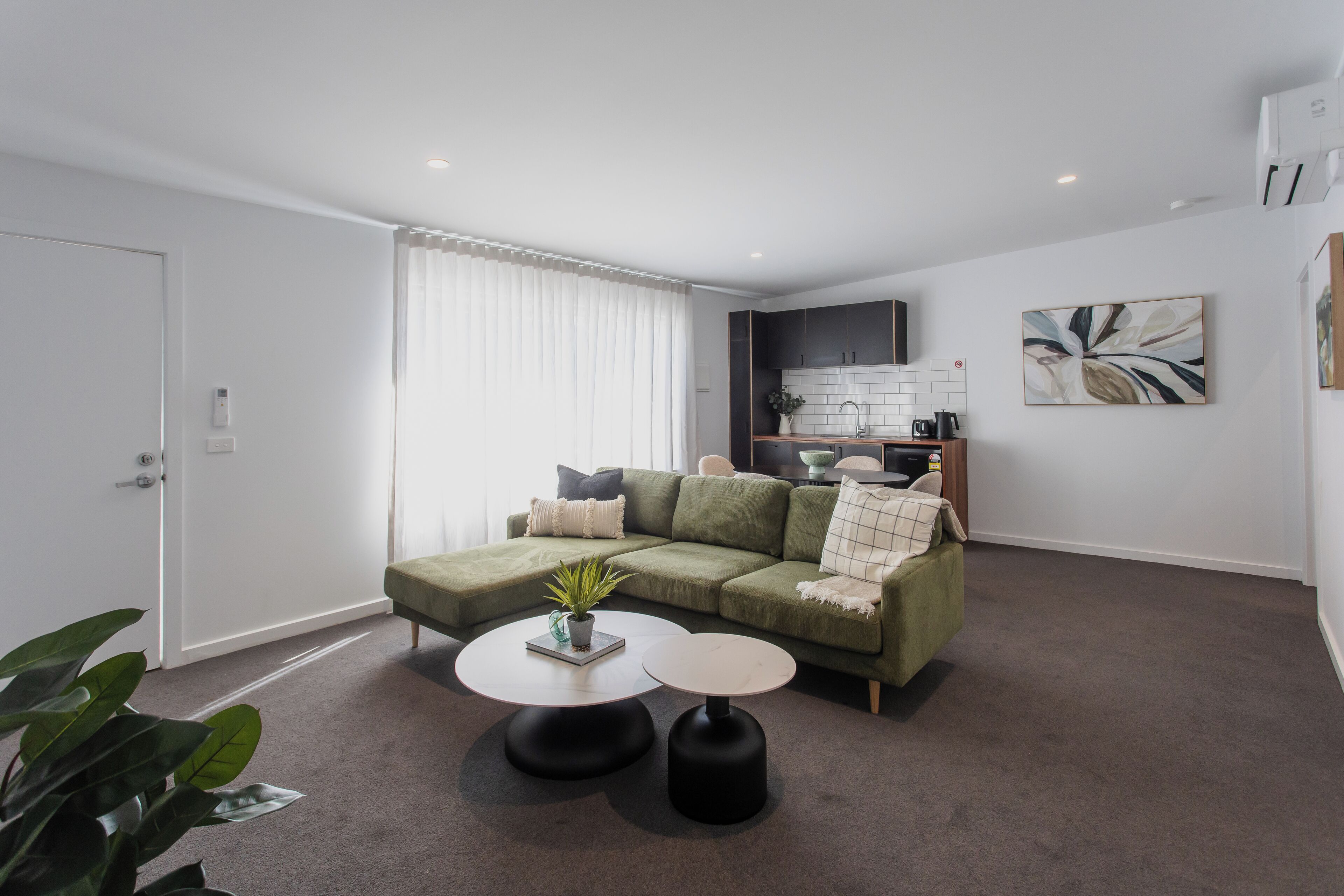 Una sala de estar moderna con un sofá verde, dos mesitas redondas y una planta en maceta.