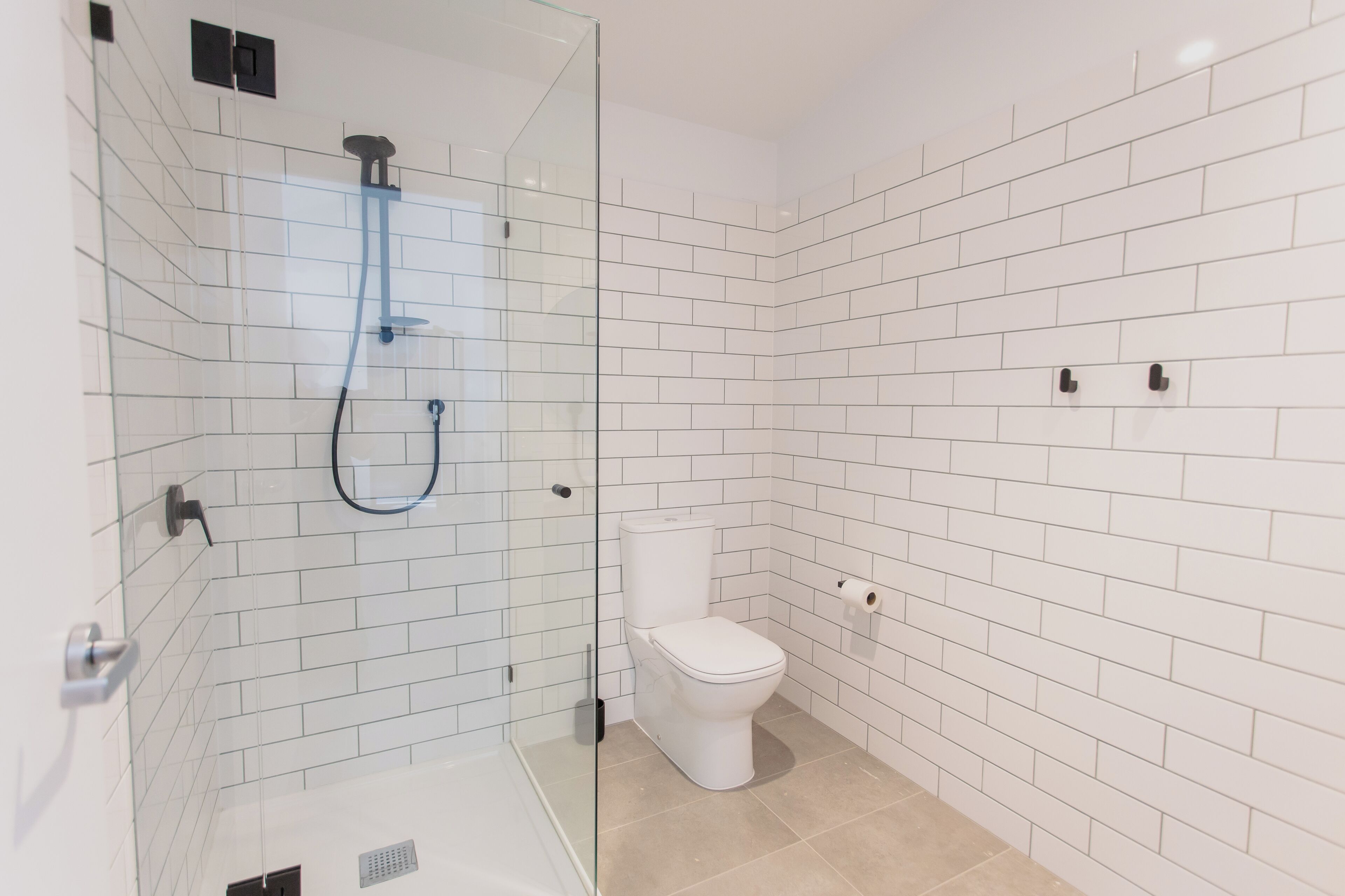 A modern bathroom with white subway tiles, a glass-enclosed shower, a white toilet, and a beige floor.