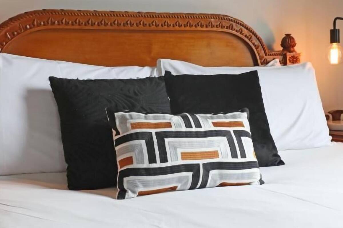 Un lit avec une literie blanche, une tête de lit en bois et deux coussins décoratifs.