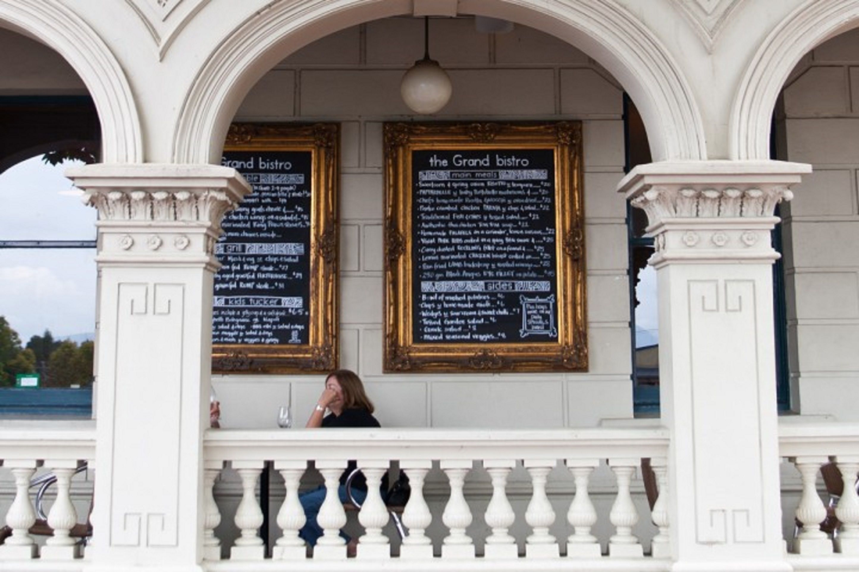 A grand bistro with ornate white columns and a balcony railing.