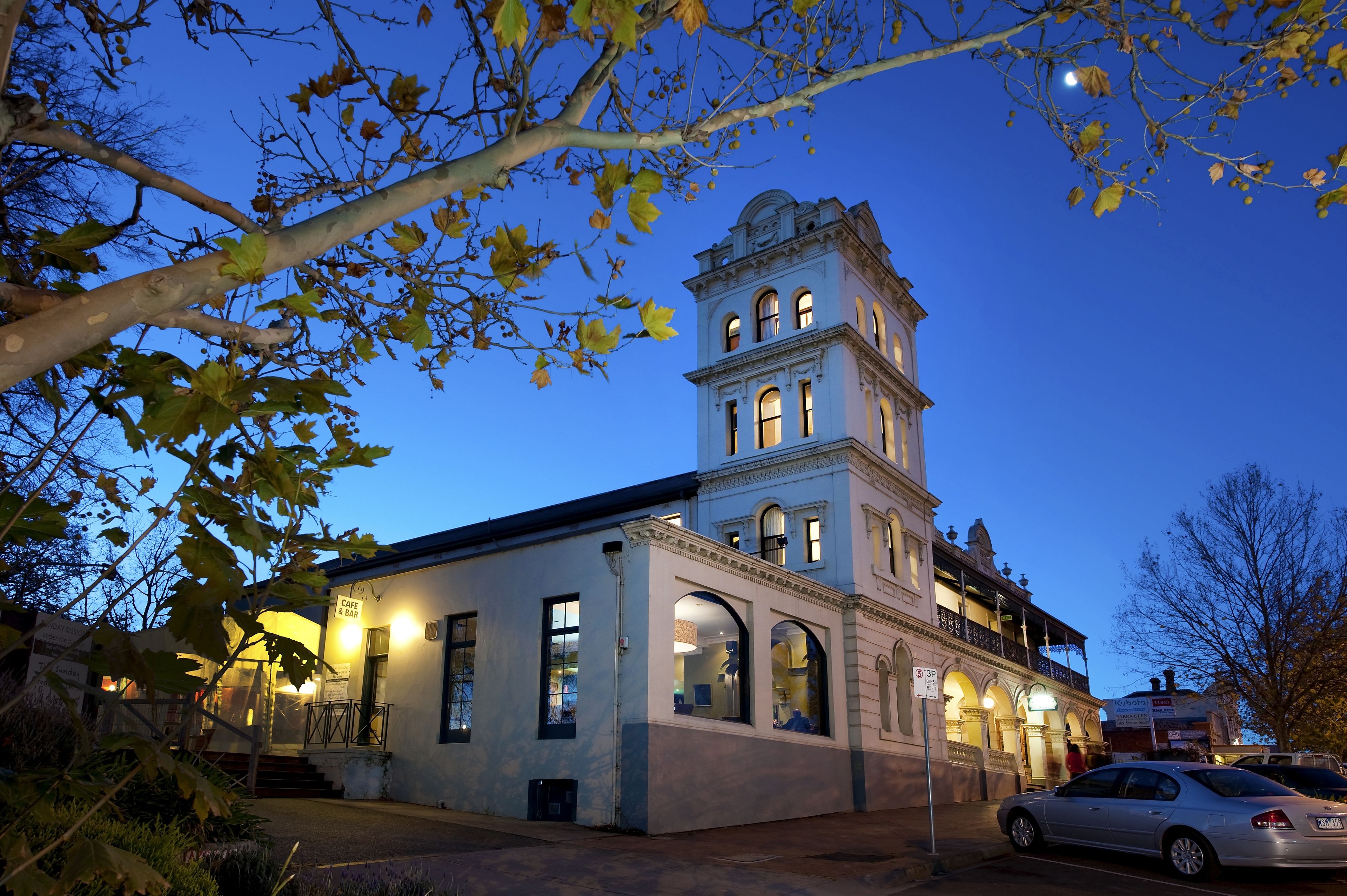 Un edificio histórico con una torre del reloj, una cafetería y un coche estacionado adelante.