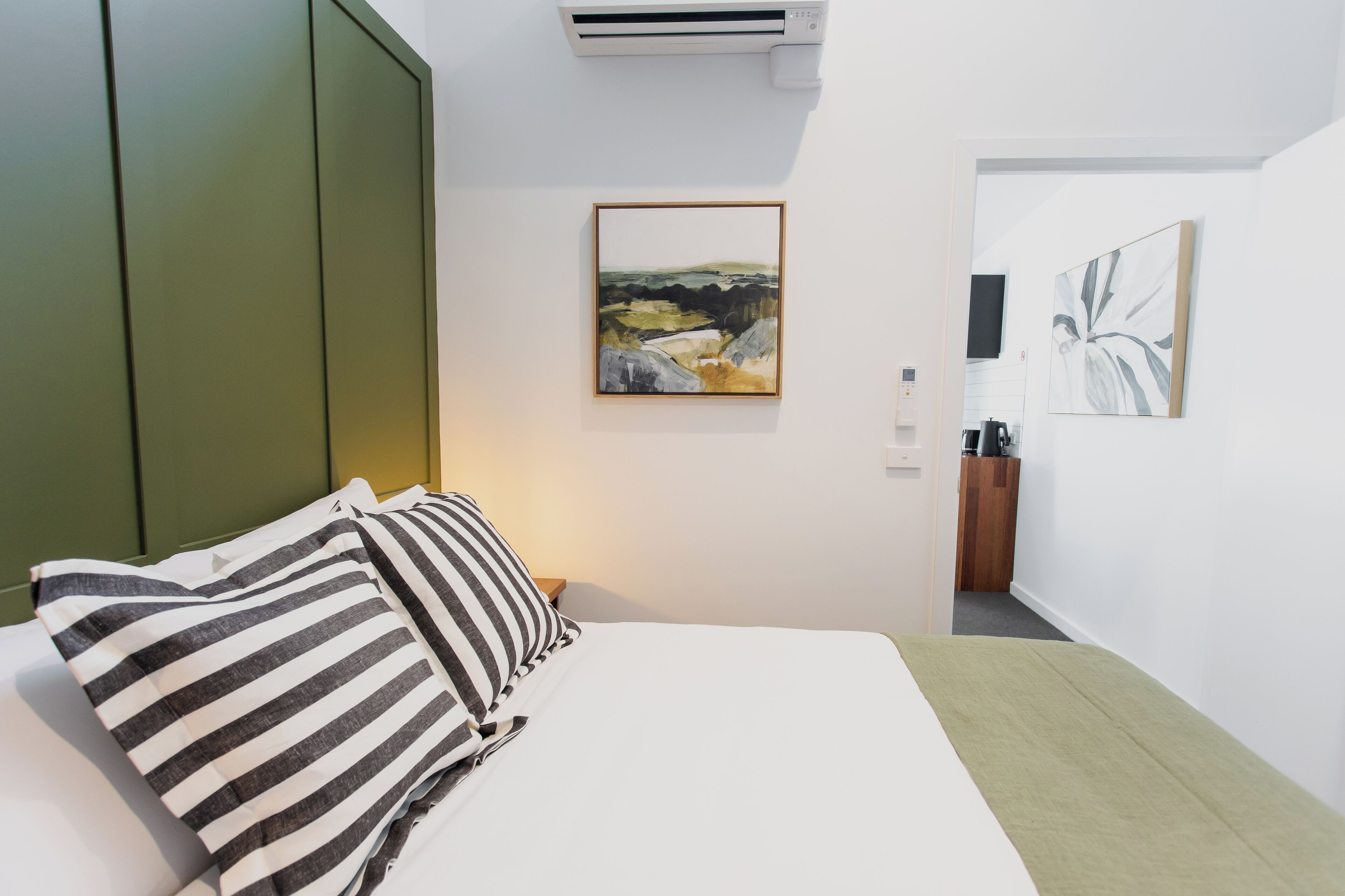 A hotel room with a bed, striped pillows, a framed landscape painting, and a coffee machine.