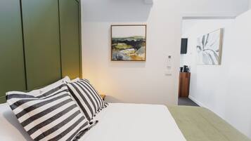 A hotel room with a bed, striped pillows, a framed landscape painting, and a coffee machine.
