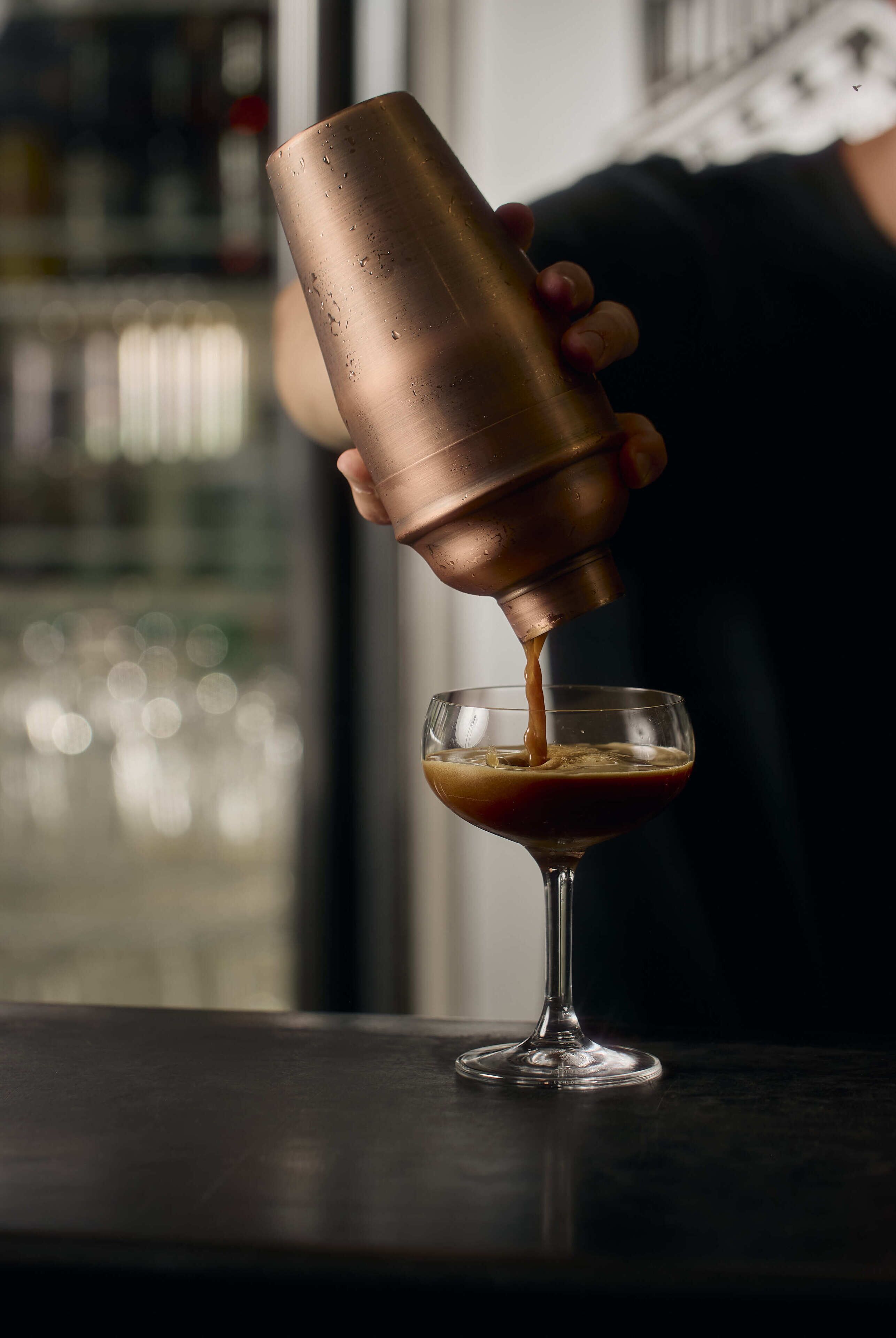 A person pouring a drink from a copper shaker into a glass.
