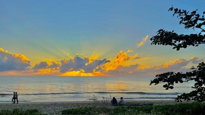 Une plage où l’on voit des gens se promener et s’asseoir, avec un coucher de soleil en arrière-plan.