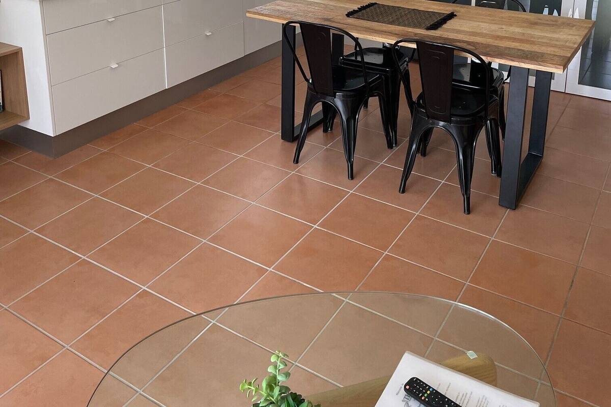 Ett modernt kök med vita skåp, ett matbord i trä och svarta stolar. På bänkskivan står en svart kaffemaskin.