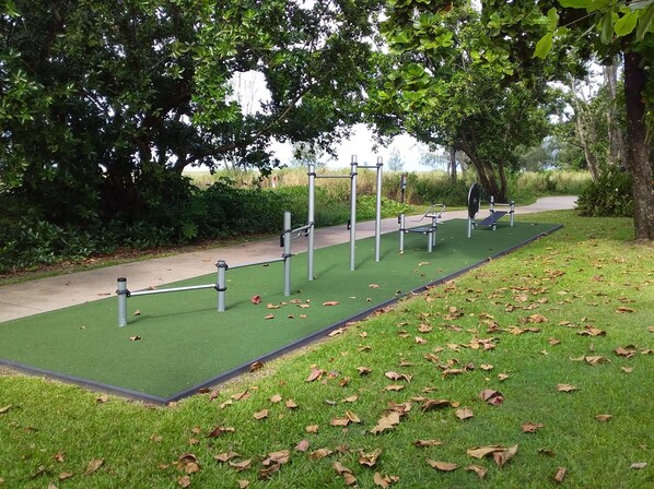 Un área de ejercicio al aire libre con césped artificial, equipamiento deportivo y un camino pavimentado.