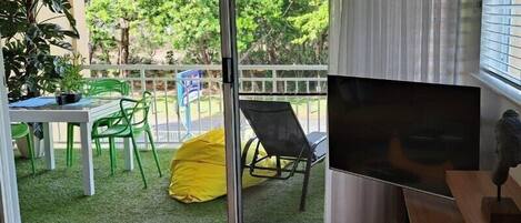 Een kamer met een schuifdeur die uitkomt op een balkon met een tafel, stoelen en een gele relaxfauteuil.