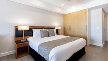 A modern hotel room with a large bed, bedside lamps, a wooden wardrobe, and a nightstand.